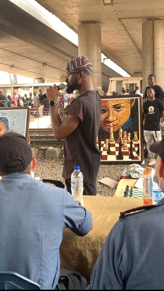 Tunde Onakoya speaking at Chess Beyond Borders, Mokola underbridge, Ibadan, with Emmanuel's chess-themed portrait on display, Emmanuel Anaiye Ifebunmi art